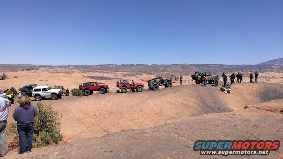 Line of off-road vehicles on a desert landscape, including a white Ford Bronco and red Jeep CJ models