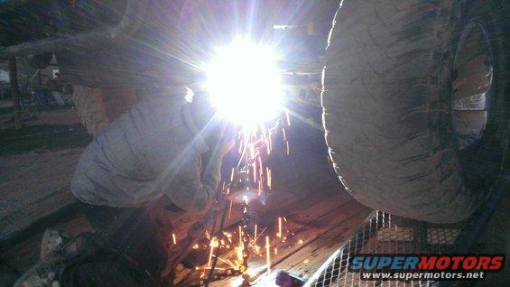 Person welding under a vehicle, sparks flying. Tires visible