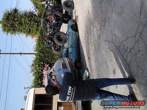 Off-road buggy on top of a teal sedan, person taking photo