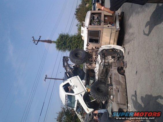 Two heavily modified off-road vehicles, one white truck and a tan RV, are entangled