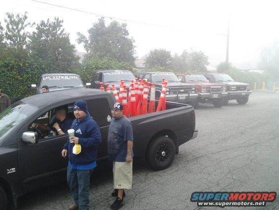 Black pickup truck bed filled with orange and white traffic cones, multiple trucks in background
