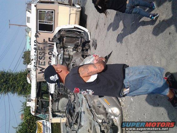 Wrecked RV with graffiti and a damaged car, people nearby