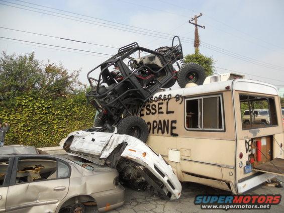 Off-road buggy atop a damaged bus, crushing two cars below