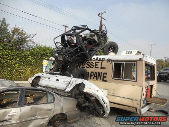 Multiple wrecked vehicles, including a UTV on top of a camper van. Text on camper reads 'SPONSORED BY VESSEL PROPANE'