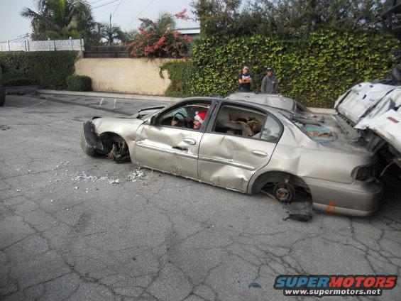 Silver sedan with all four wheels missing, significant body damage, and a person wearing a Santa hat inside