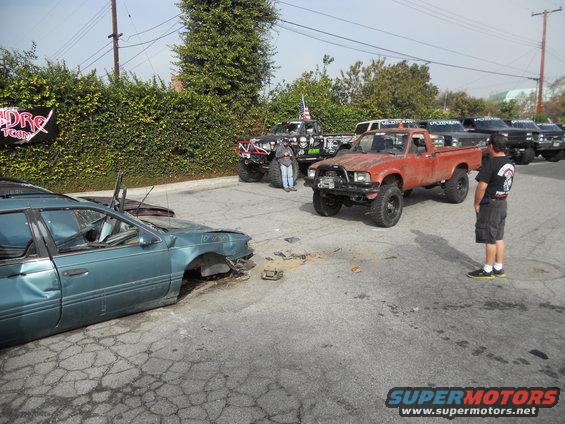 Orange pickup truck with a rusty front end and large tires parked on cracked asphalt
