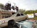 1986 Ford Bronco - Junkyard scene shows a buggy on a trailer, a man standing on a sedan, and other cars piled up.