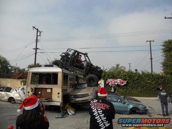 off-road buggy on top of a bus with other wrecked cars around, people in Santa hats