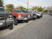 1986 Ford Bronco - A line of modified trucks, including a red Chevrolet and a black GMC, are parked on a street.