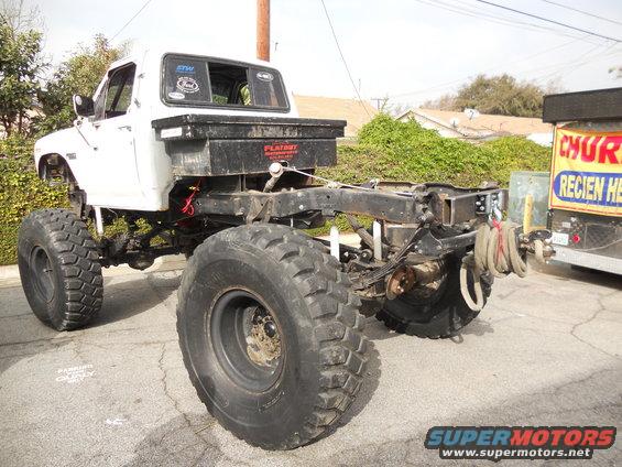 Rear chassis of a white pickup truck with oversized tires and a toolbox