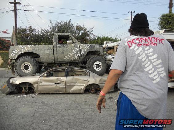 Mud-splattered pickup truck with large tires on a crushed gold sedan