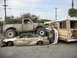 1986 Ford Bronco - A heavily modified pickup truck has crushed a sedan, with a bus visible in the background. Text on the bus indicates sponsorship by 'WESSEL…