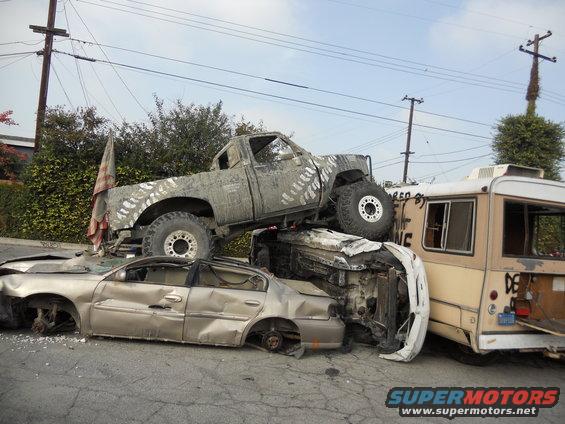 truck on top of crushed cars next to a bus