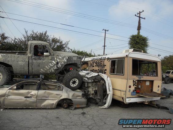 Damaged vehicles piled up: a pickup truck on a sedan, next to a bus