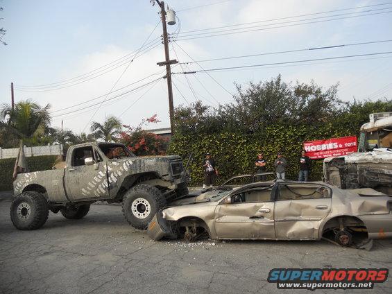 Lifted pickup truck on top of a wrecked sedan. "Hobbies & Toys" banner visible