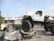 1986 Ford Bronco - A heavily modified white pickup truck is shown crushing a car, with a driver behind the wheel.