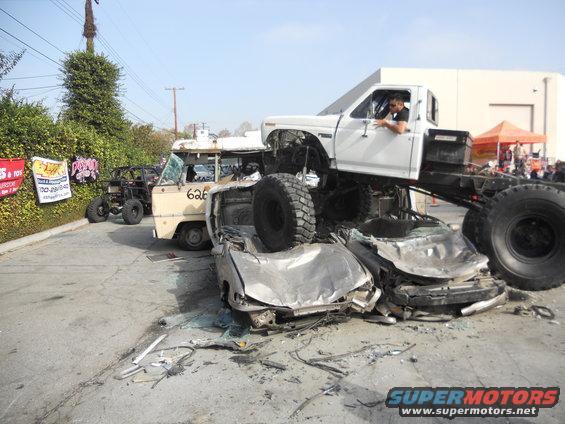 White pickup truck crushing cars, with a van and ATV in the background
