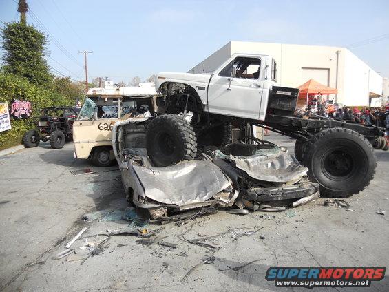 Monster truck on top of crushed cars, with a van and buggy in background