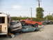 1986 Ford Bronco - Multiple vehicles are stacked and damaged in a junkyard setting.