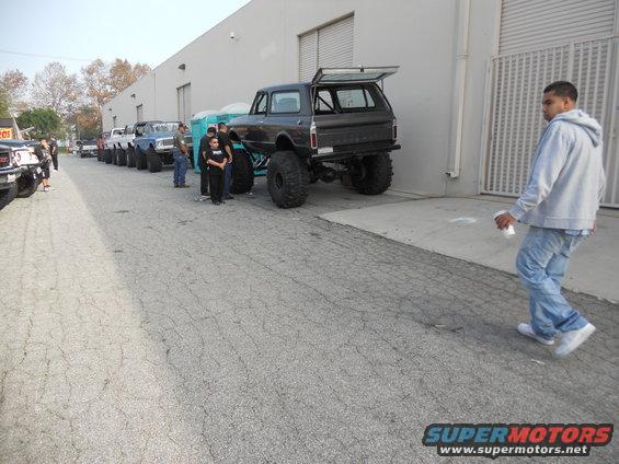 Several lifted SUVs and trucks are parked in a line outside a building. A man walks away from the camera