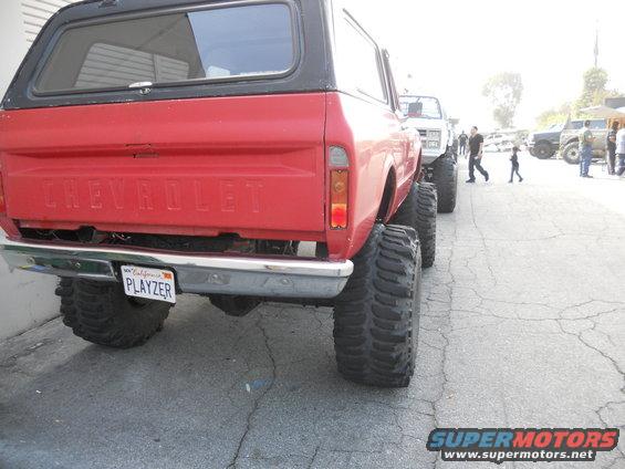 Red Chevrolet K5 Blazer rear view, lifted with large off-road tires and a black camper shell