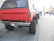 1986 Ford Bronco - A line of lifted off-road vehicles, including a red Chevrolet K5 Blazer, are parked on a street.