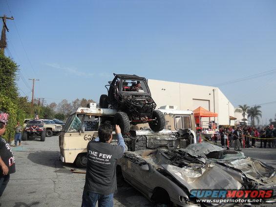 Buggy on top of crushed cars and a van, crowd watching