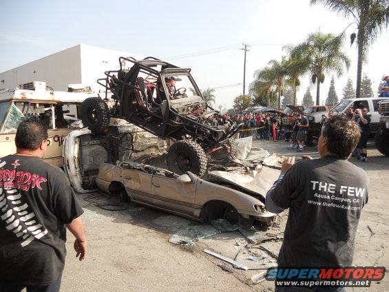 Off-road buggy atop a crushed car, with spectators watching