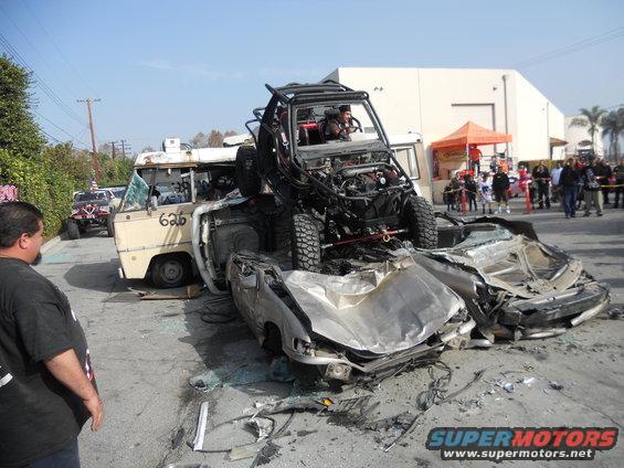 off-road buggy on top of two wrecked cars, with a van behind it and people watching