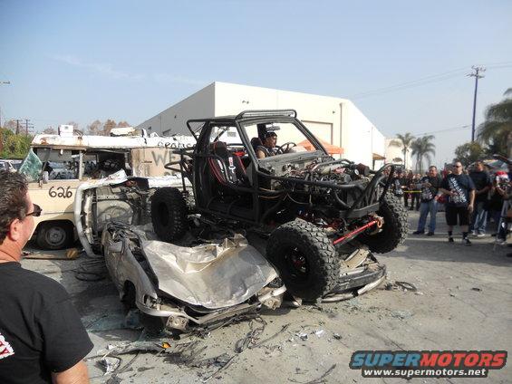 Off-road buggy on crushed car, with a damaged van in background