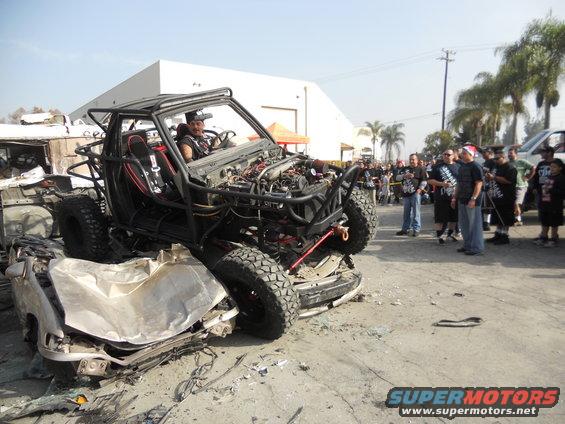 Custom off-road buggy with exposed engine crushing a car