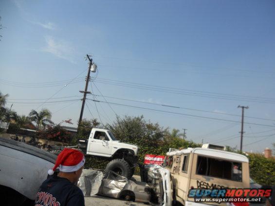 White pickup truck with large tires, lifted, with a person in a Santa hat in the foreground