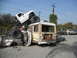 1986 Ford Bronco - A white pickup truck is precariously balanced on a bus, which is itself crushing several cars.