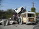 1986 Ford Bronco - A chaotic scene shows a modified pickup truck precariously perched atop a bus, with a car crushed beneath them.