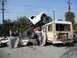 1986 Ford Bronco - A chaotic scene with a monster truck crushing a bus and car, surrounded by onlookers.