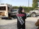 1986 Ford Bronco - A collection of damaged vehicles and a person observing the scene, with a large off-road truck in the background.