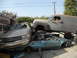 1986 Ford Bronco - A heavily modified panel van is piled on top of two heavily damaged sedans in a junkyard.