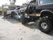 1986 Ford Bronco - A lifted 1986 Ford Bronco is parked on top of a wrecked sedan, with other vehicles in the background.