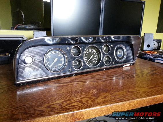 Vehicle dashboard cluster with multiple gauges, including speedometer and tachometer. It has a chrome bezel