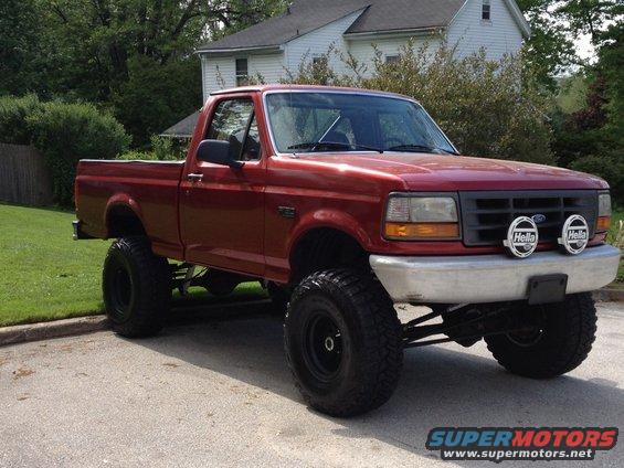 Red pickup truck with lifted suspension and large tires, viewed from a 3/4 front angle