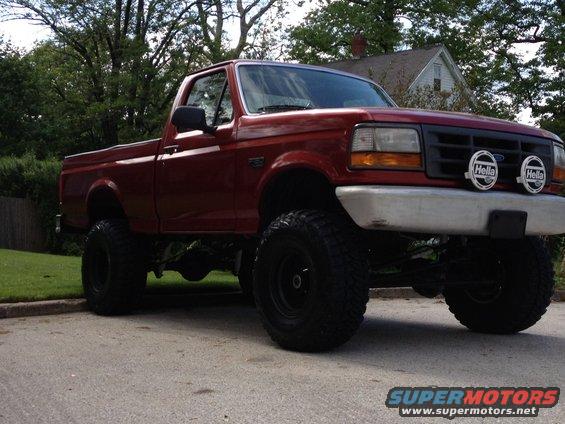Red 1996 Ford F-150 pickup truck with large tires and Hella lights
