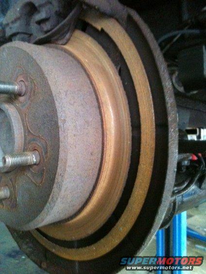 Close-up of a rusty rear brake rotor with brake pads visible