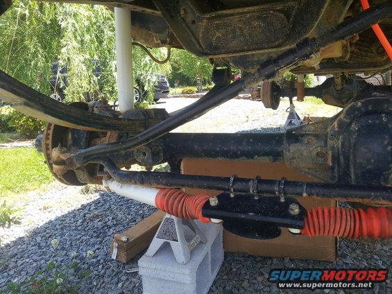 Undercarriage view showing suspension parts, a shock absorber with orange boot, and a second vehicle in the background