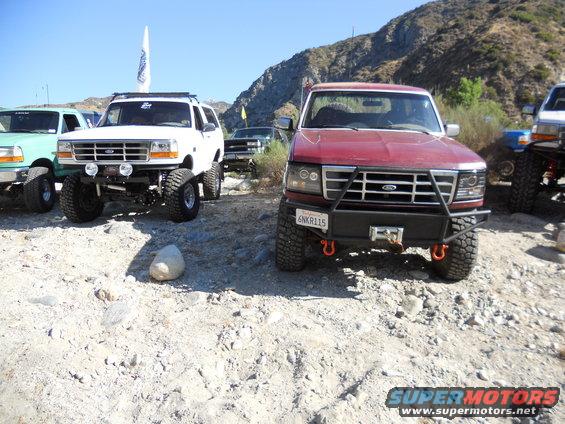 Red 1992-1996 Ford Bronco front end with aftermarket bumper and winch, parked next to a white lifted Bronco