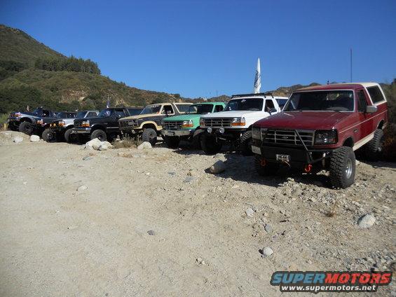 Several Ford Broncos and F-Series trucks parked on a dirt lot with hills in the background