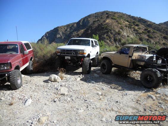 Three modified off-road vehicles parked on a rocky, arid hillside under a clear blue sky