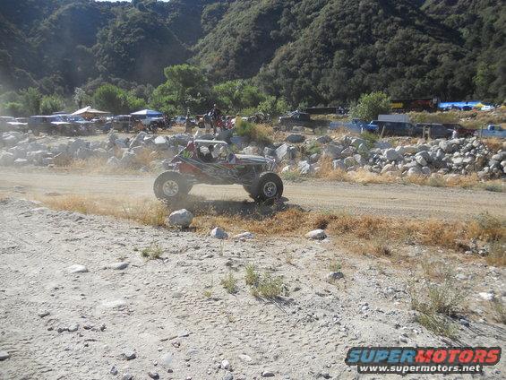 Off-road buggy kicking up dust on a dirt track with other vehicles in background