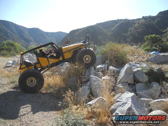 Yellow custom buggy with large tires navigating a rocky trail, two people visible inside