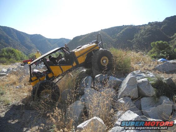 Yellow off-road buggy climbing over large rocks in a dry creek bed