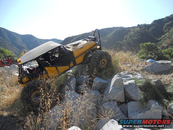 Yellow off-road vehicle with a roll cage navigating a rocky terrain
